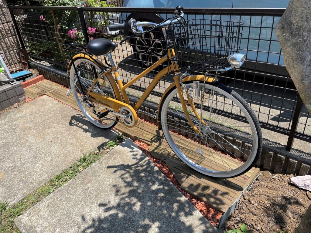 MUKUタイルをカットして変形地にきれいに並べ、駐輪スペースが完成した。黄色の自転車が停まっている。