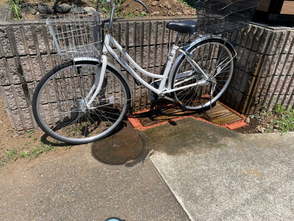 MUKUタイルをカットして変形地にきれいに並べ、駐輪スペースが完成した。白色の自転車が停まっている。
