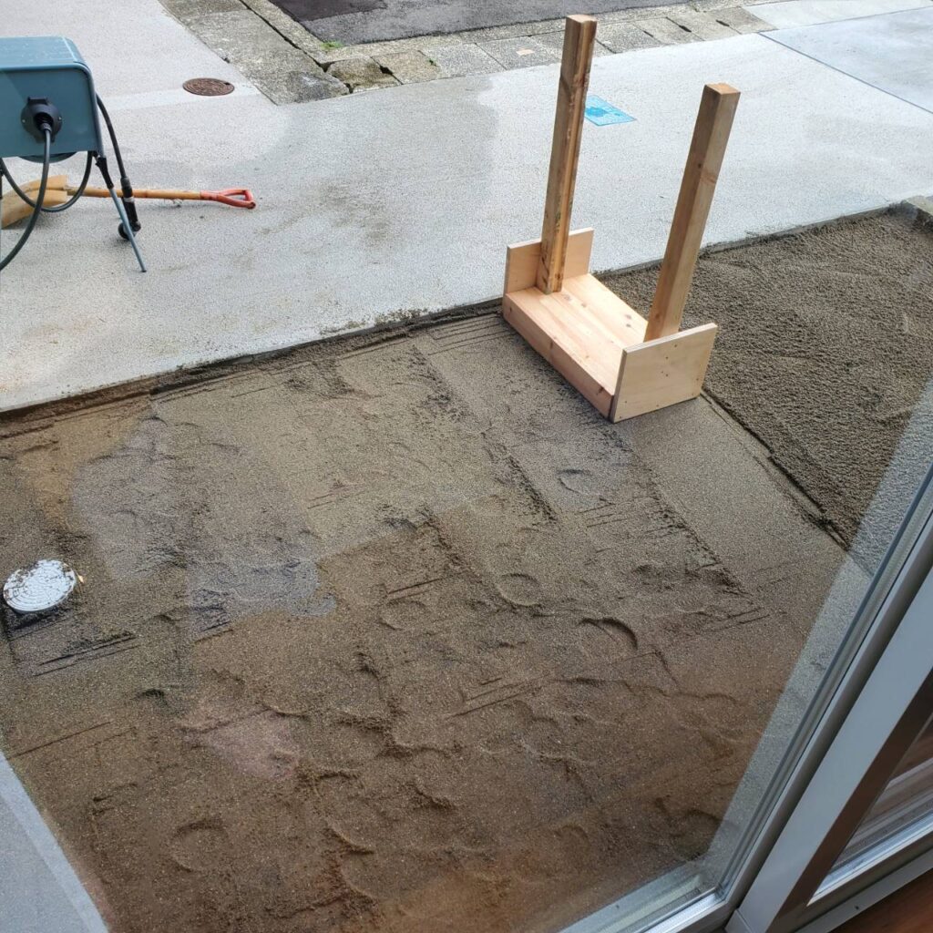 お庭のDIYで下地作りをする様子。手作りタンパーで砂を転圧している。