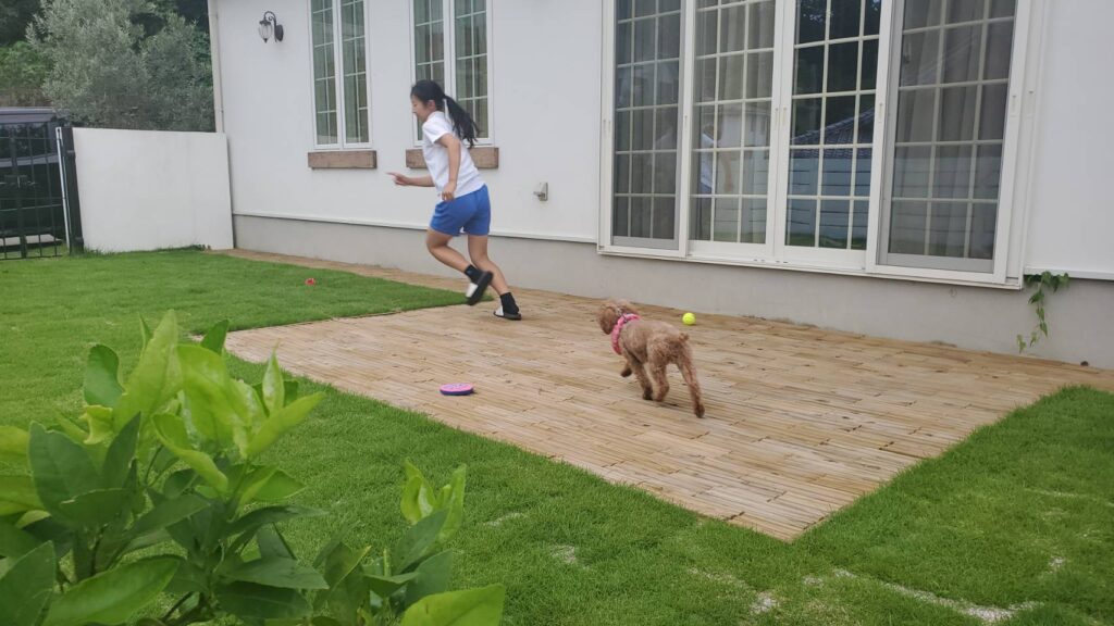 DIYしたお庭のウッドタイルの上で走る女の子と犬